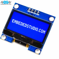 Bottom/connector side of a monochrome OLED display module, showing the blue PCB, exposed pin solder joints, surface-mount components, and ribbon cable connector interface.