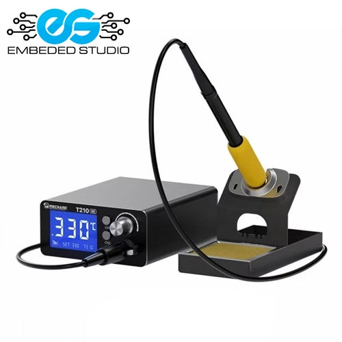 A compact black MC T210 SE thermostatic soldering station with a bright blue digital temperature display showing 330, paired with a soldering iron stand holding a yellow-accented iron handpiece, featuring the Embeded Studio logo on a white background.
