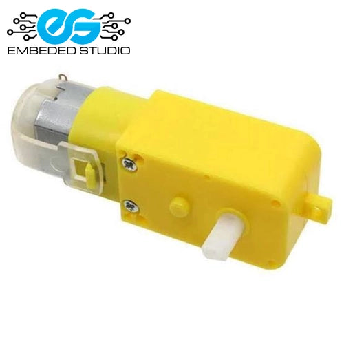 A yellow plastic TT DC gear motor with a white output shaft and a transparent plastic cover over the motor terminals, displayed next to the Embeded Studio logo.